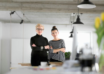 2 femmes bras croisés devant un plan de travail, l'une d'âge mur cheveux blancs courts, l'autre plus jeune brune chignon