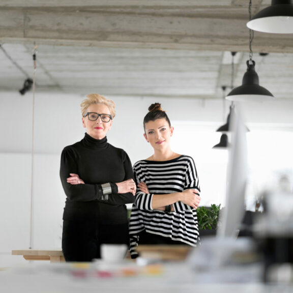 2 femmes bras croisés devant un plan de travail, l'une d'âge mur cheveux blancs courts, l'autre plus jeune brune chignon