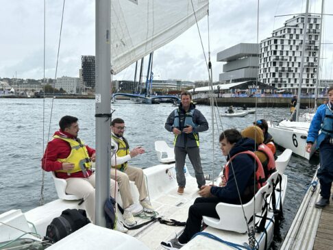 Photo d'un groupe de jeunes bénéficiaires de l'OCIRP, sur le bateau imoca partage, avec François Guiffant, assis et souriants